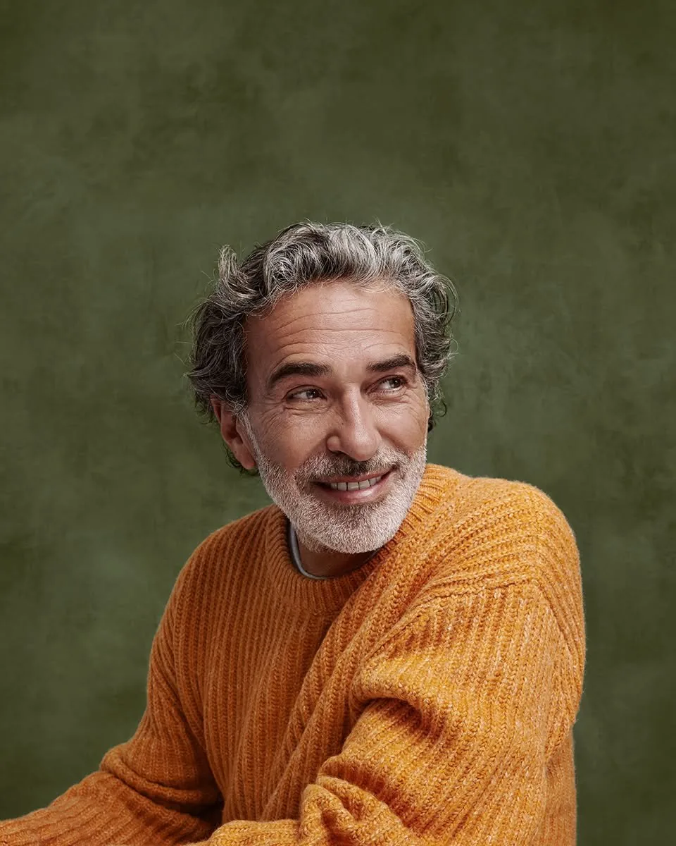 Homme aux cheveux gris en pull orange, assis devant un fond orange uni