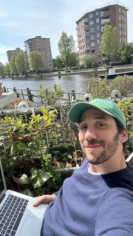 Ma photo de départ&nbsp;: selfie sur un balcon, pull bleu, casquette verte, ordinateur sur les genoux
